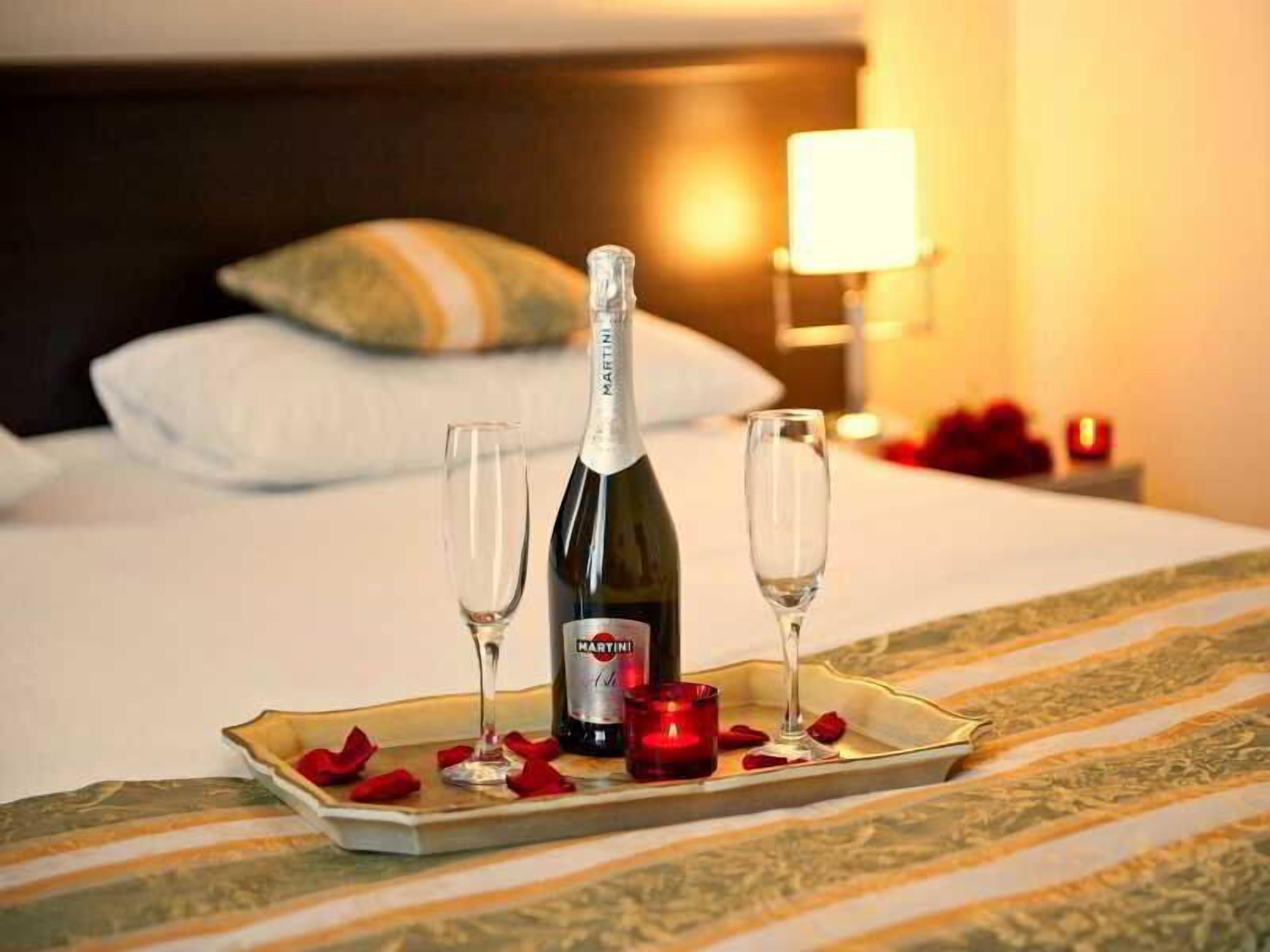 A bed with a tray of champagne, two glasses, and rose petals.