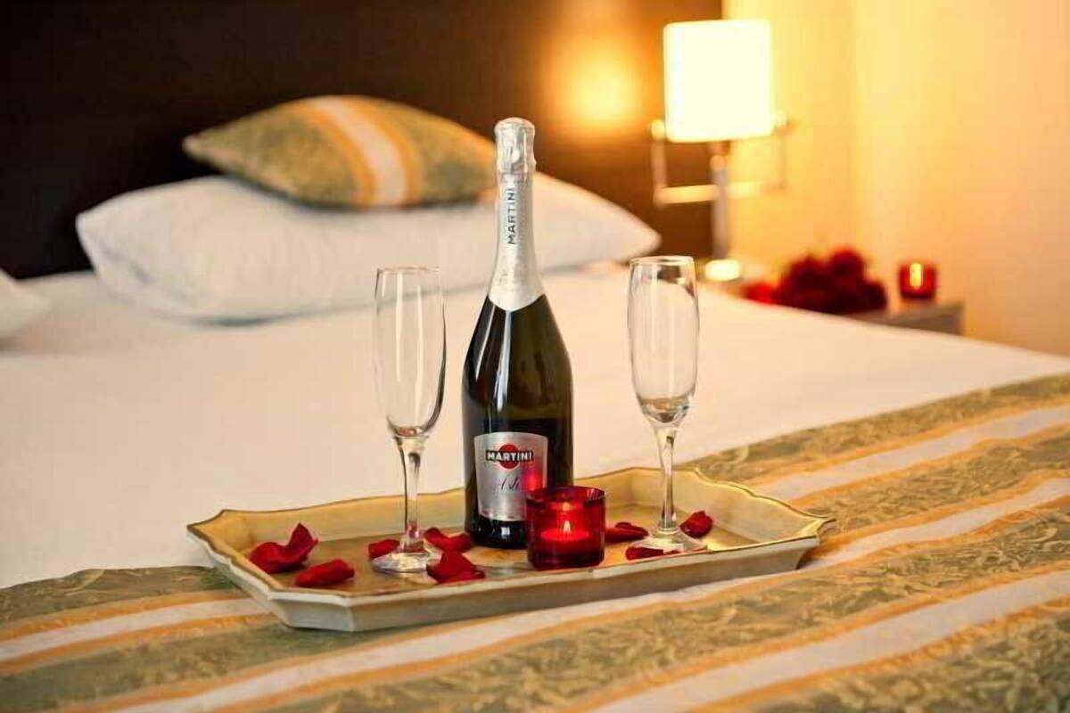 A bed with a tray of champagne, two glasses, and rose petals.