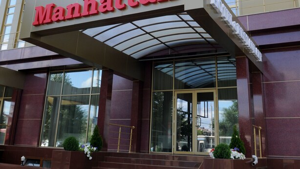 Een hotelingang met een opvallend 'Manhattan' bord, grote glazen ramen en een modern architectonisch ontwerp.