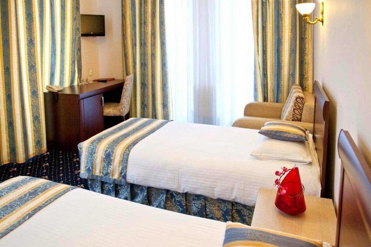 A hotel room with two beds, a desk, a TV, and curtains.
