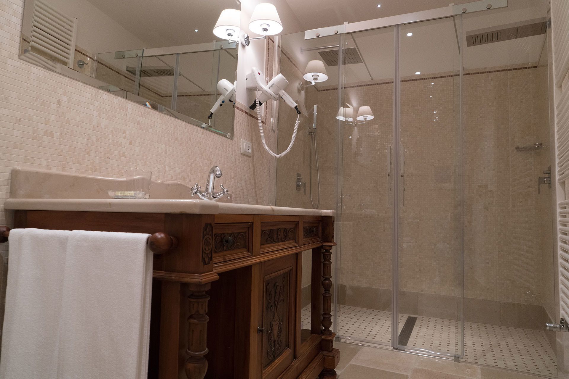 A modern bathroom with a glass shower enclosure, a wooden vanity with a mirror, and a white towel on the counter.