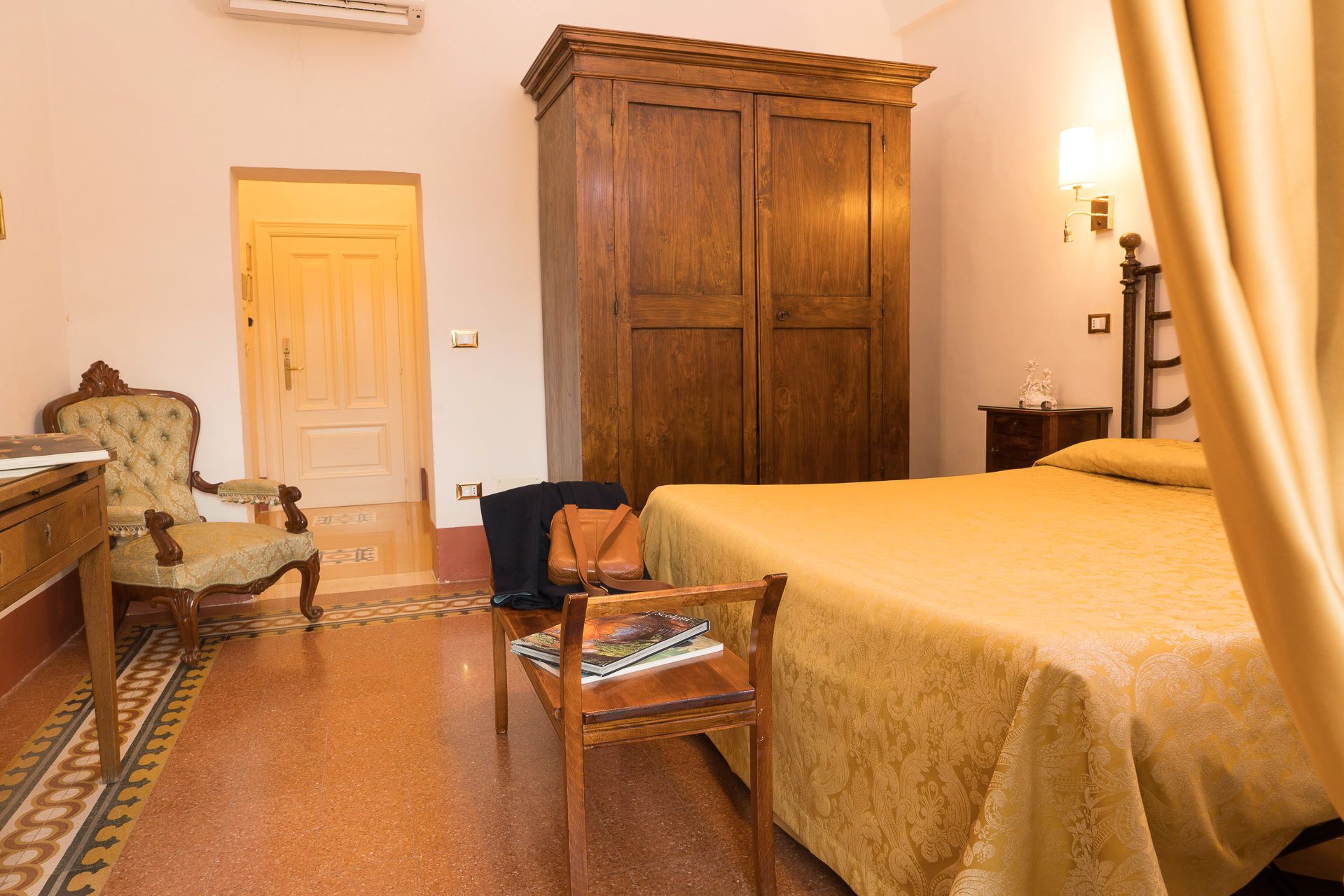 Ein Hotelzimmer mit Bett, Holzschrank, Stuhl, Schreibtisch und Lampe.