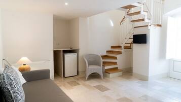 Un salon moderne comprenant un canapé, une petite table, un fauteuil, un escalier et un téléviseur fixé au mur.
