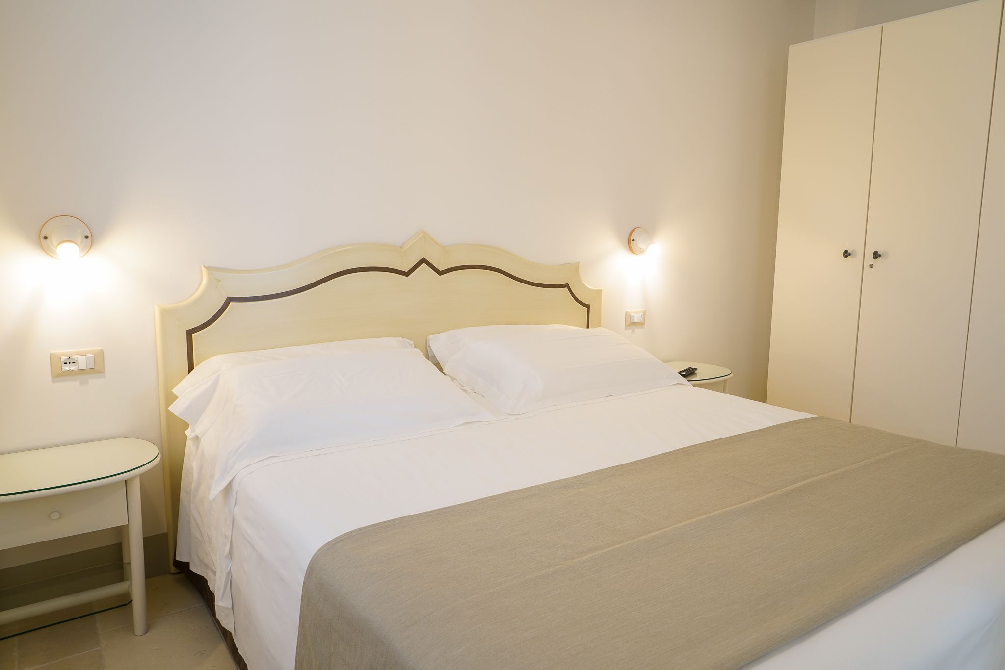 Una cama bien hecha con tablero de madera, dos mesitas de noche y un armario.