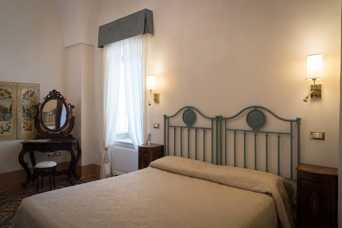 Una camera d'albergo ben ordinata con un letto, una cassettiera, uno specchio e due lampade a parete.