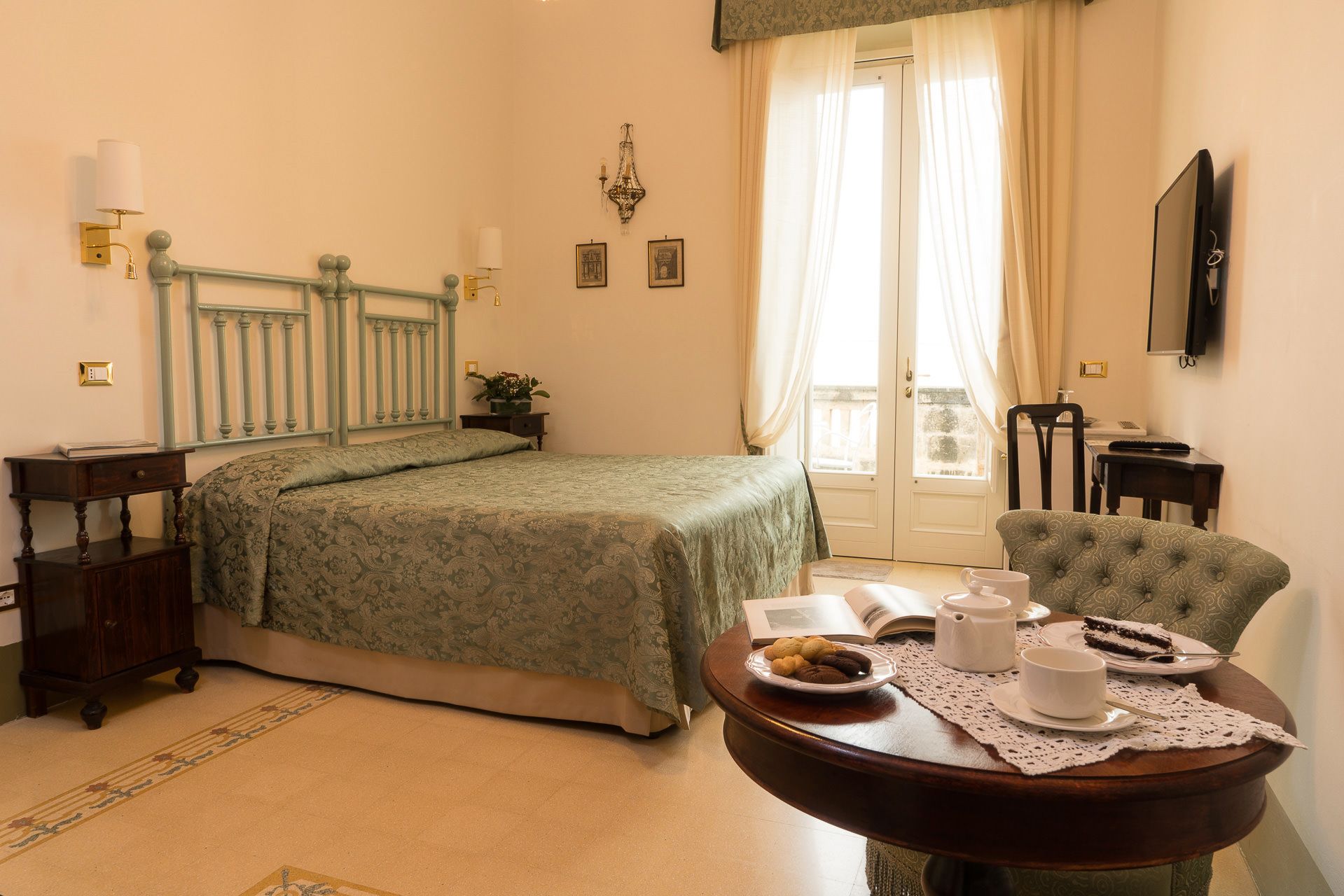 A bedroom with a bed, bedside table, chair, and a small table with a plate of cookies and a cup.