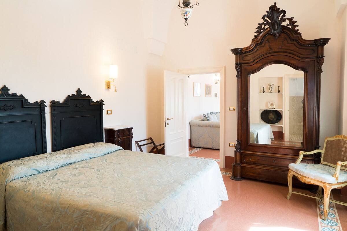 Una camera da letto con un letto grande, un armadio in legno, una sedia e uno specchio.