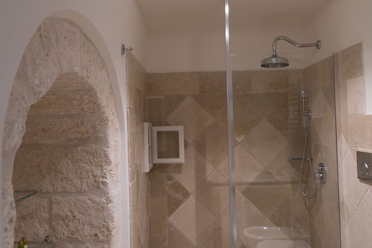 Een douche met een glazen deur, een douchekop en een bedieningspaneel aan de muur.