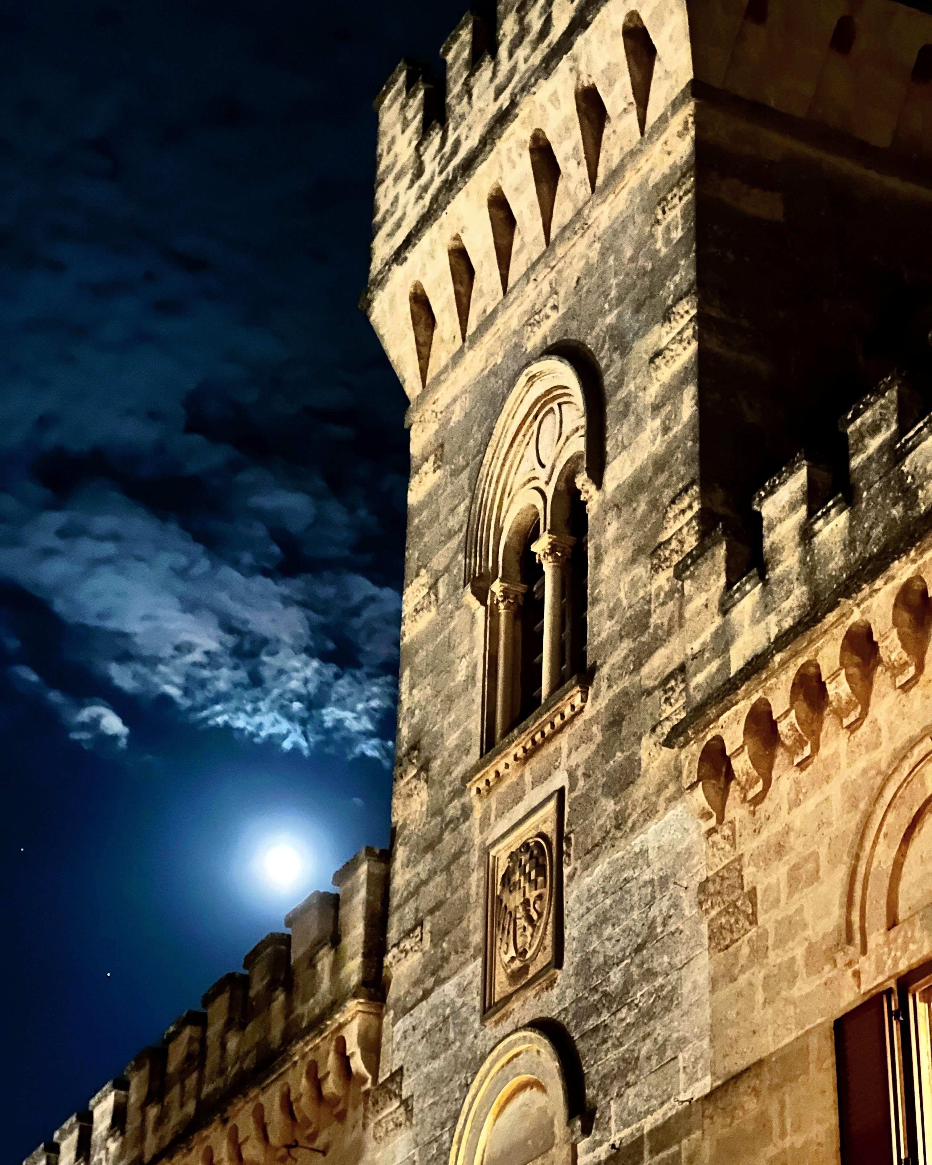 A stone building with arched windows and a moon in the sky.