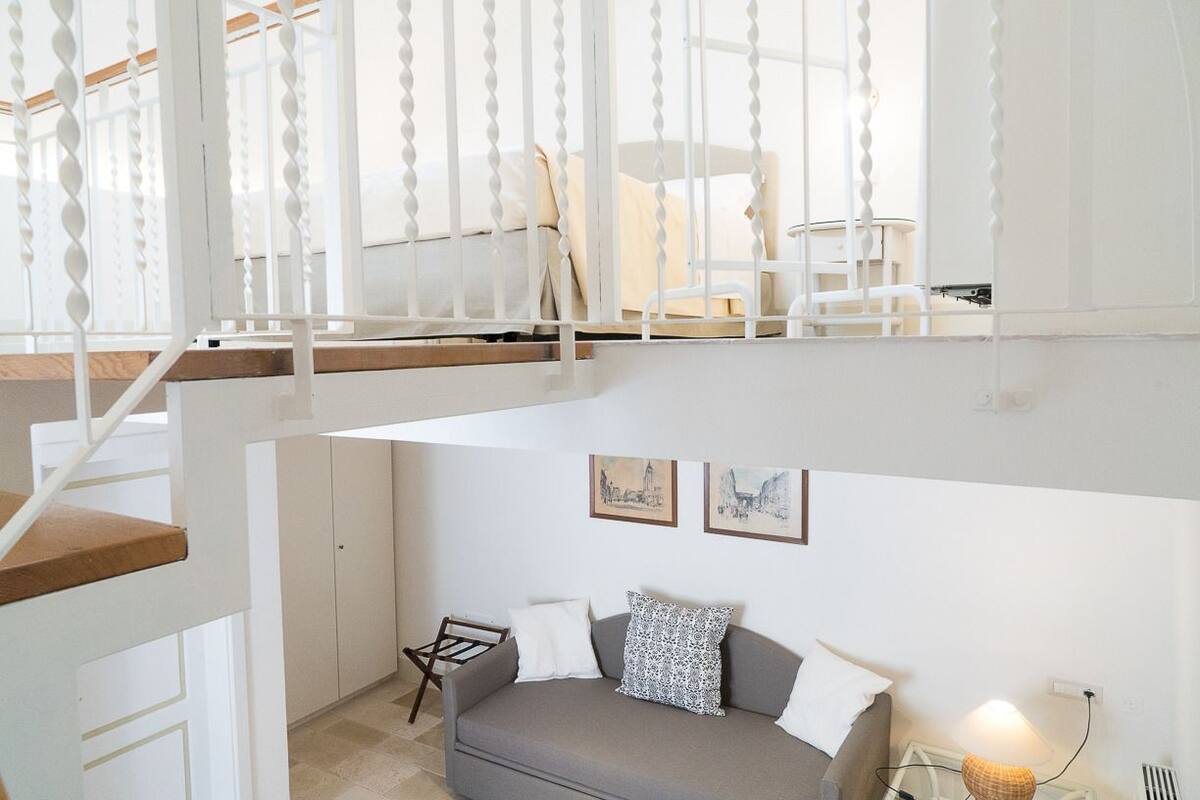 Un interno moderno con un divano grigio, cuscini bianchi e due quadri appesi al muro.