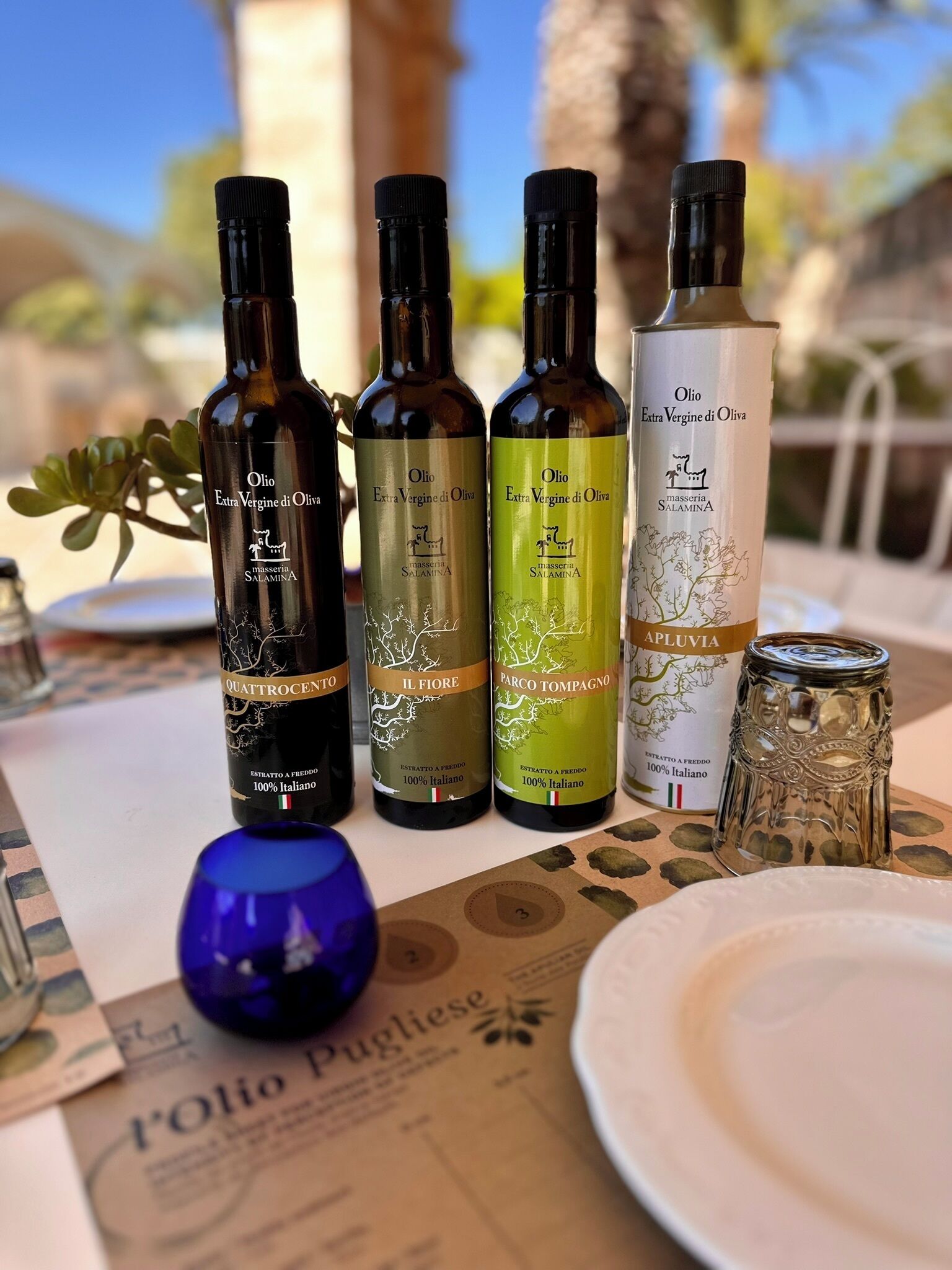 Four bottles of extra virgin olive oil and a glass jar on a table with a menu.