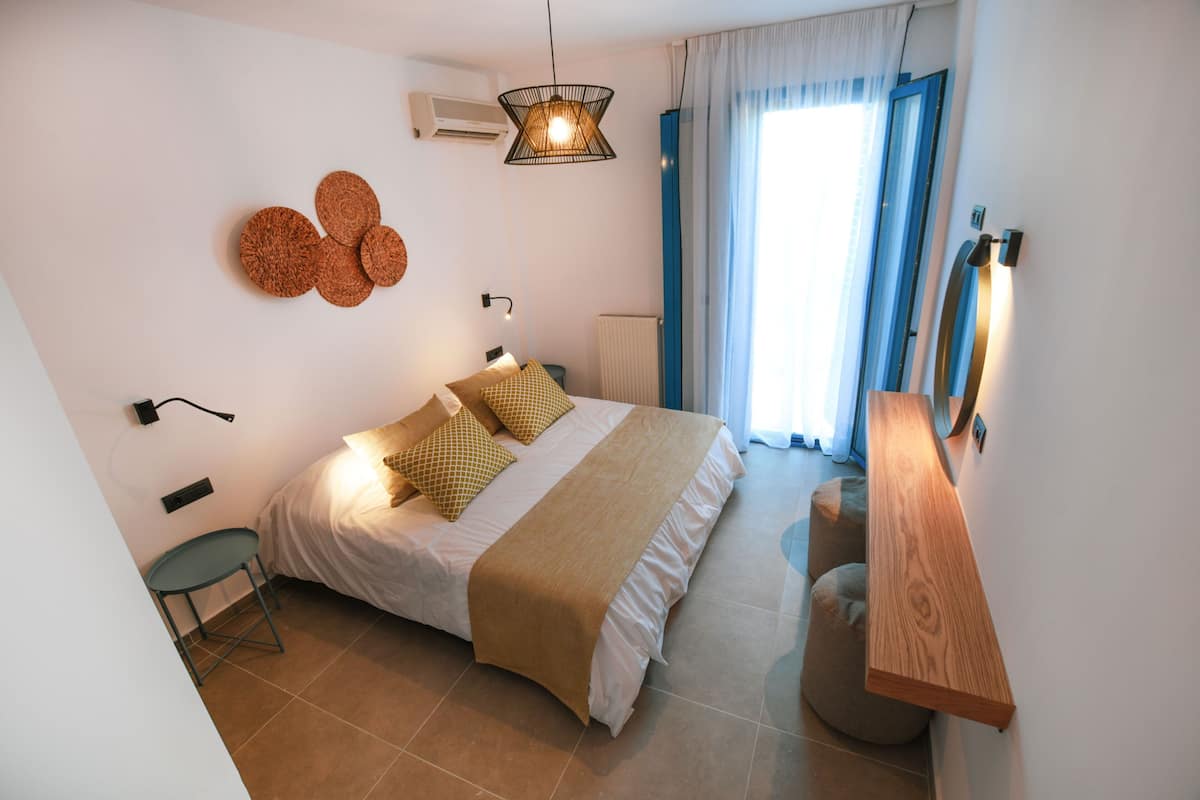 A modern bedroom with a bed, bedside tables, a chair, a hanging light fixture, and a window with curtains.