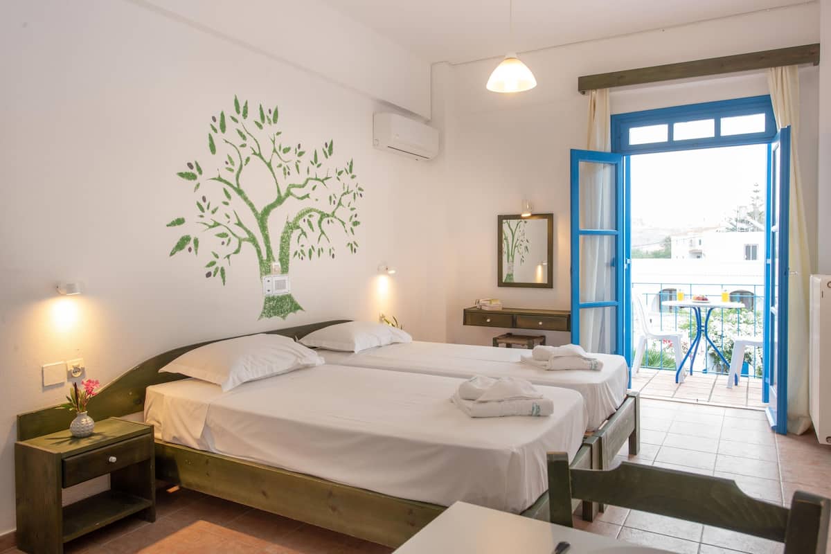 A room with two beds, a small table, a chair, a wall-mounted mirror, and a balcony with a table and chairs.