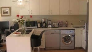 A compact kitchen with a dishwasher, washing machine, and a small dining area. - Navona Constantia Guest Cottage (Cape Town)