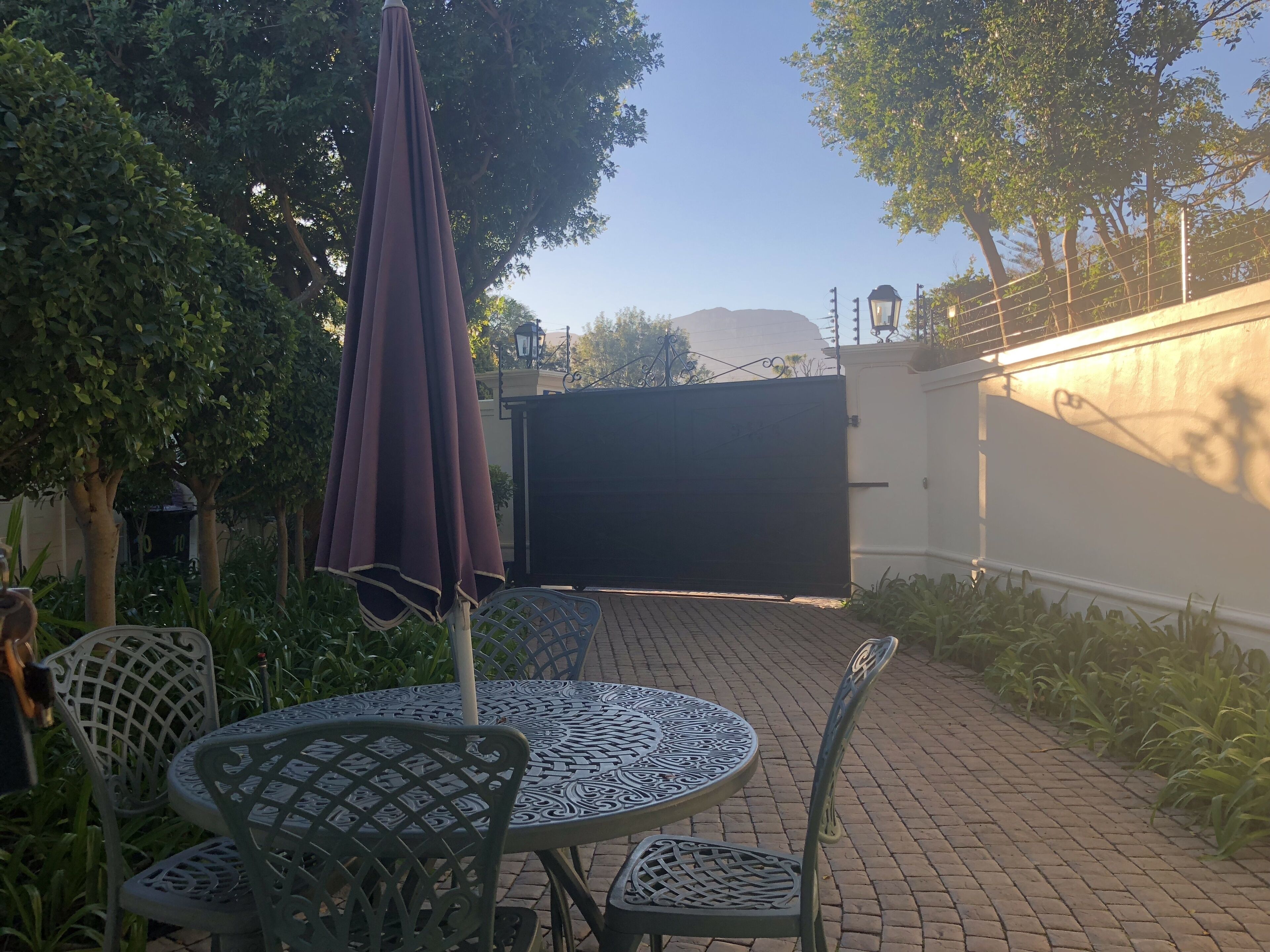 Un espace patio avec une table ronde et des chaises, un parasol violet et une porte en arrière-plan.