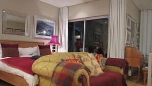 A hotel room with a large bed, a sofa, a desk, and a view of the outside through a glass door. - Navona Constantia Guest Cottage (Cape Town)