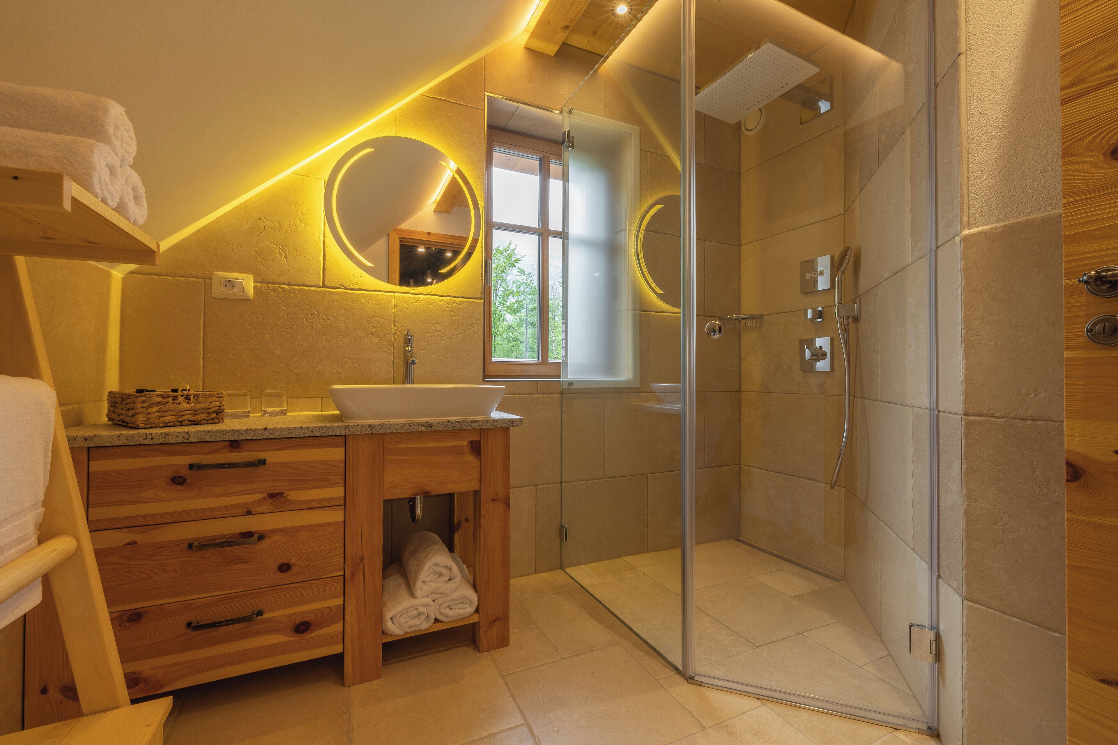 A modern bathroom with a glass-enclosed shower, wooden vanity, and two round mirrors with illuminated frames.