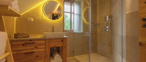 Un baño moderno con ducha de vidrio, tocador de madera y dos espejos redondos con marcos iluminados.