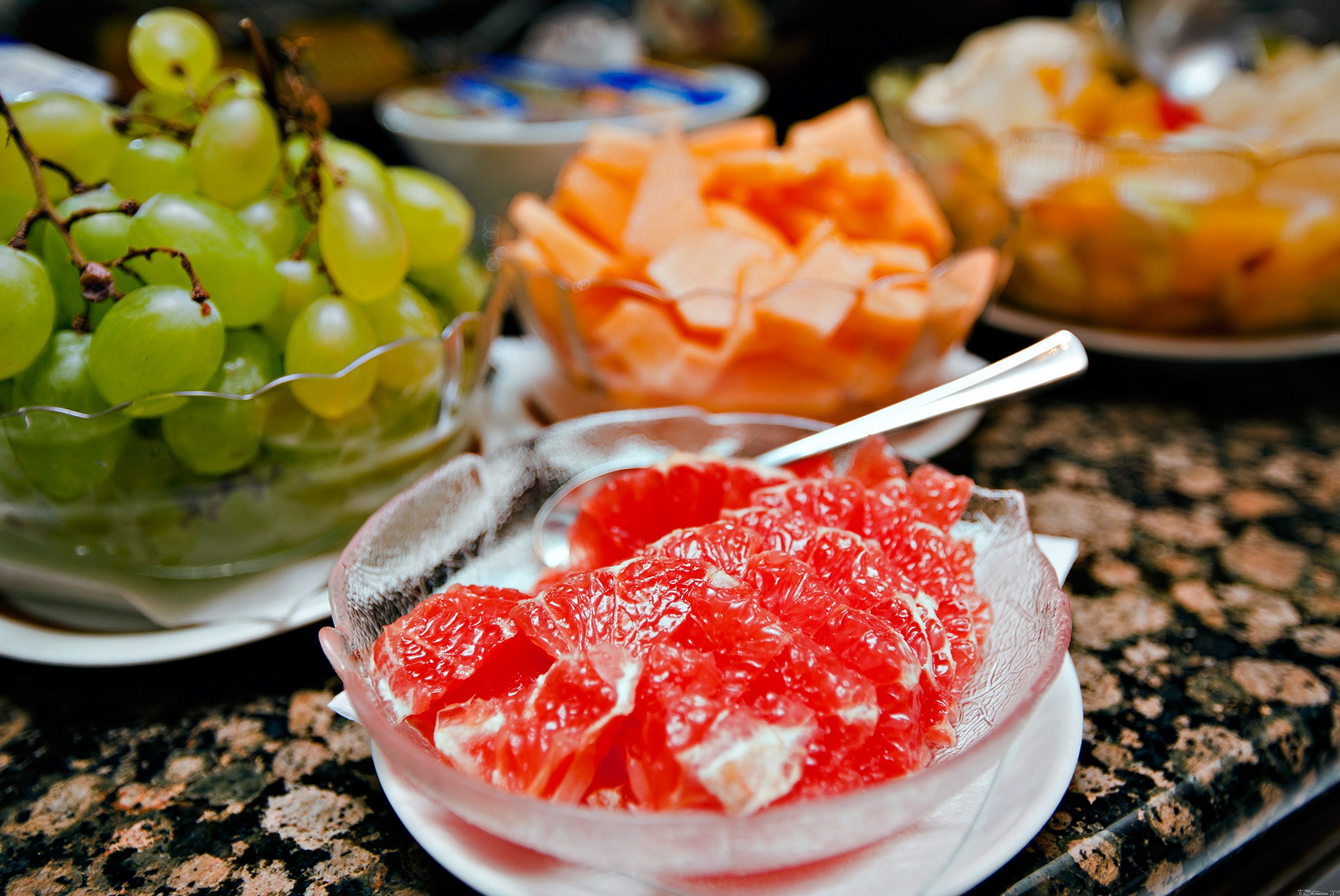 A table with a bowl of green grapes, a bowl of sliced oranges, and a bowl of red fruit.