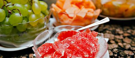 A table with a bowl of green grapes, a bowl of sliced oranges, and a bowl of red fruit.