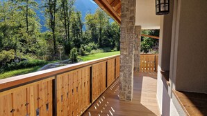 A wooden balcony with a stone pillar, a view of a forested area, and a hanging plant rail. - PRIVILLAGE STARE - B&B, Villa and Chalet Resort (Bohinj)