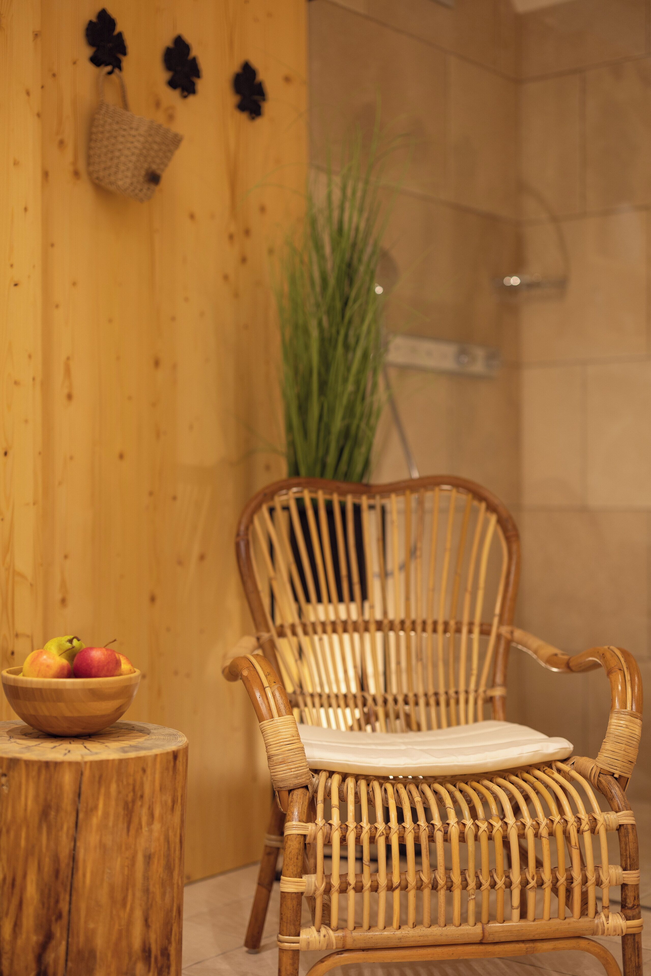 A wicker chair with a woven seat and backrest, positioned next to a wooden wall with a small wooden stool holding a bowl of fruit.