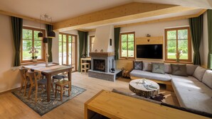 A spacious living room with a wooden ceiling, a fireplace, a sofa, a dining table with chairs, and large windows with curtains. - PRIVILLAGE STARE - B&B, Villa and Chalet Resort (Bohinj)
