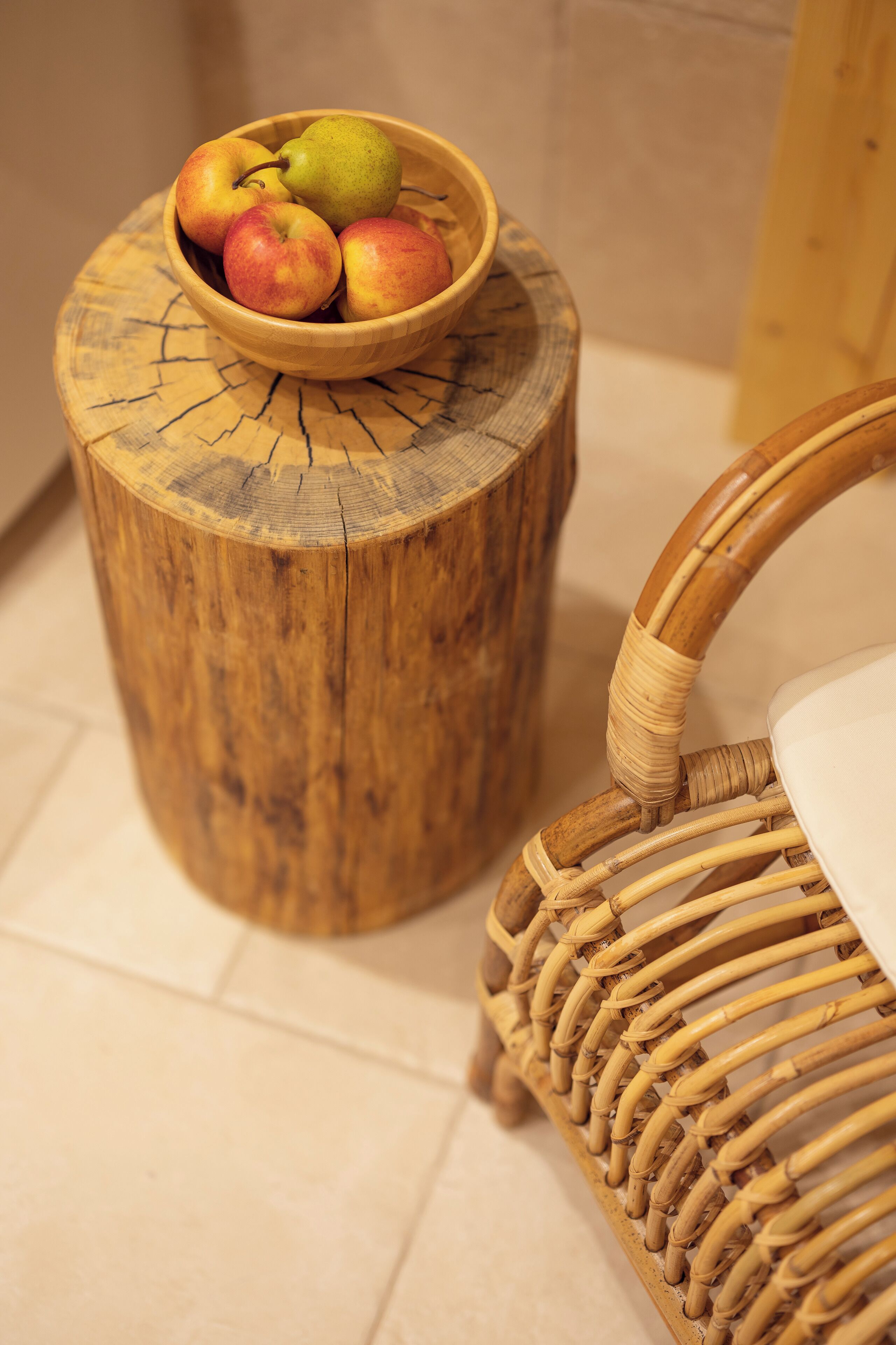 A wooden stool with a bowl of fruit and a wicker chair.