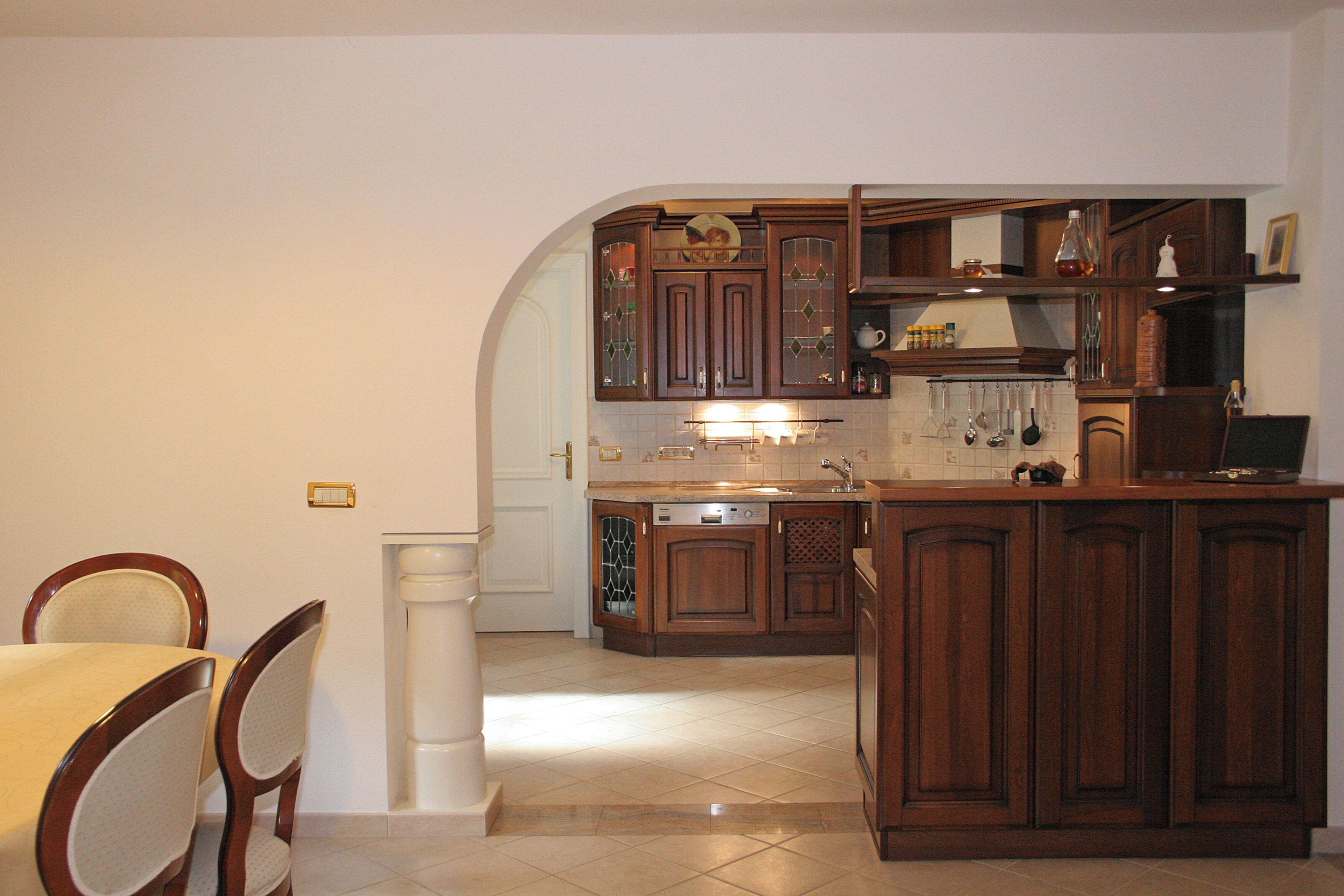 A kitchen with wooden cabinets, a dining table with chairs, and a tiled floor.