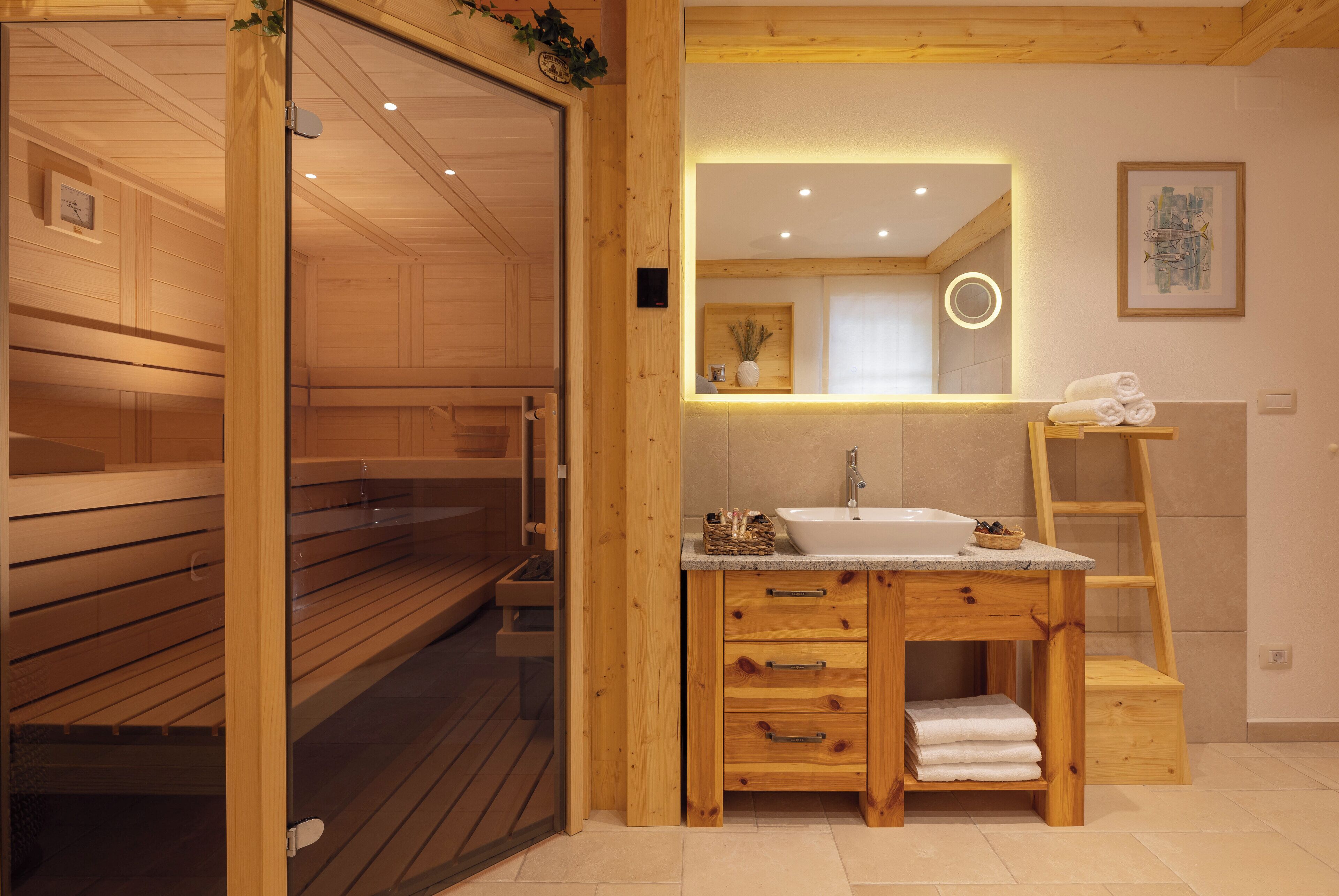 A wooden sauna room with benches, a wooden vanity with a sink, and a mirror with a circular light.