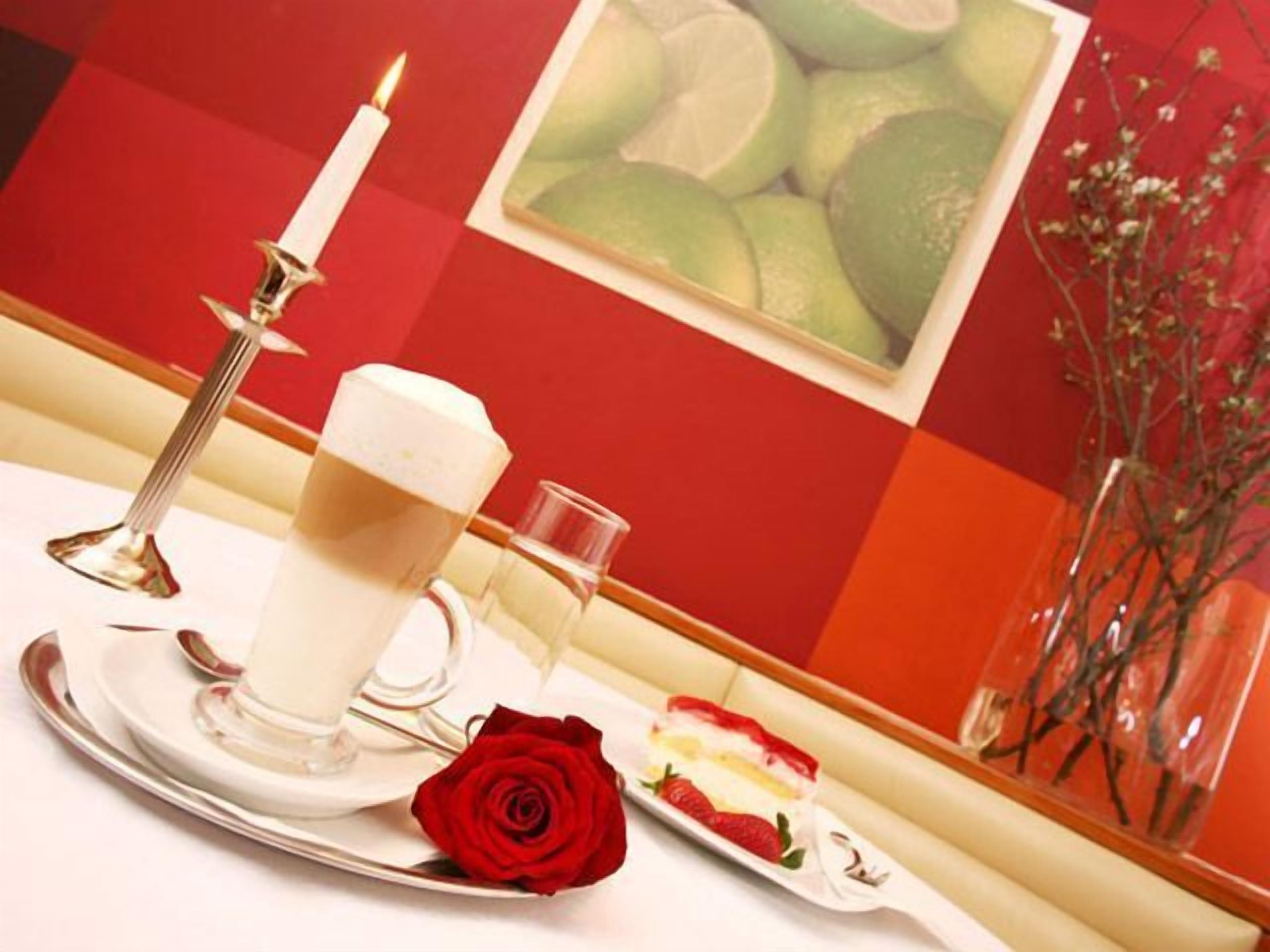 Ein Esstisch mit Kerze, einem Glas Wasser, einer Kuchenscheibe und einer roten Rose.