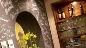 Eine Bar mit einer Tafelwand, einem Blumentopf und Regalen mit Flaschen und Gläsern.