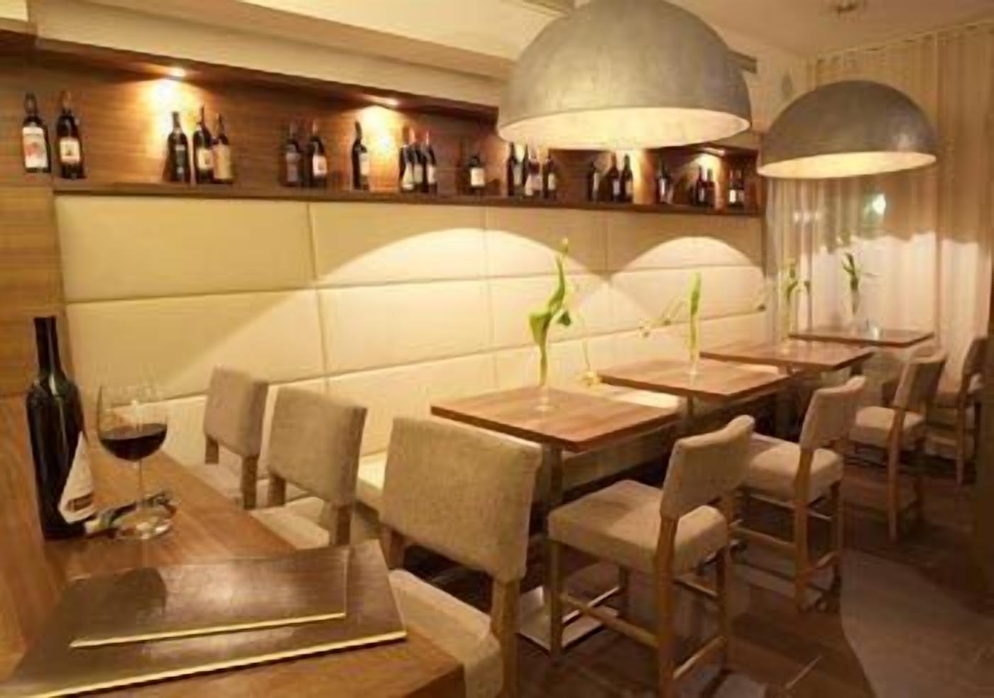 Un restaurante con mesas y sillas de madera, una estantería para vinos en la pared e iluminación colgante.