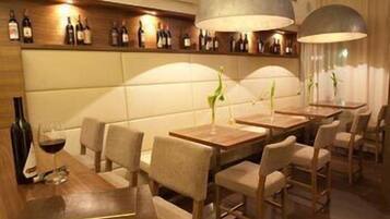 Un restaurante con mesas y sillas de madera, una estantería para vinos en la pared e iluminación colgante.