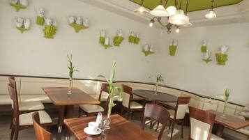 Interior de un restaurante con mesas y sillas de madera, decoración de pared verde y lámparas colgantes.
