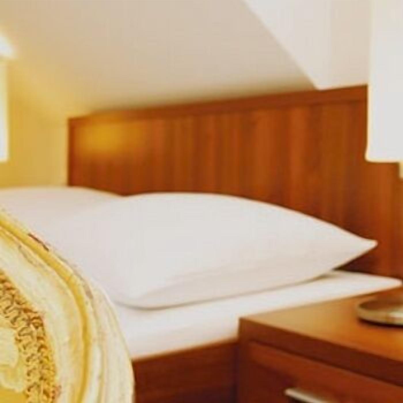 A hotel room with a wooden headboard, a bed with white bedding, and a nightstand with a lamp.