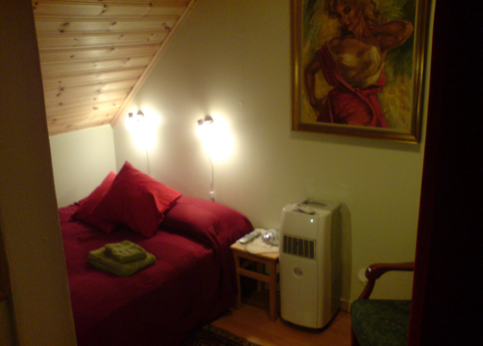 A bedroom with a red bed, a heater, and a painting on the wall.