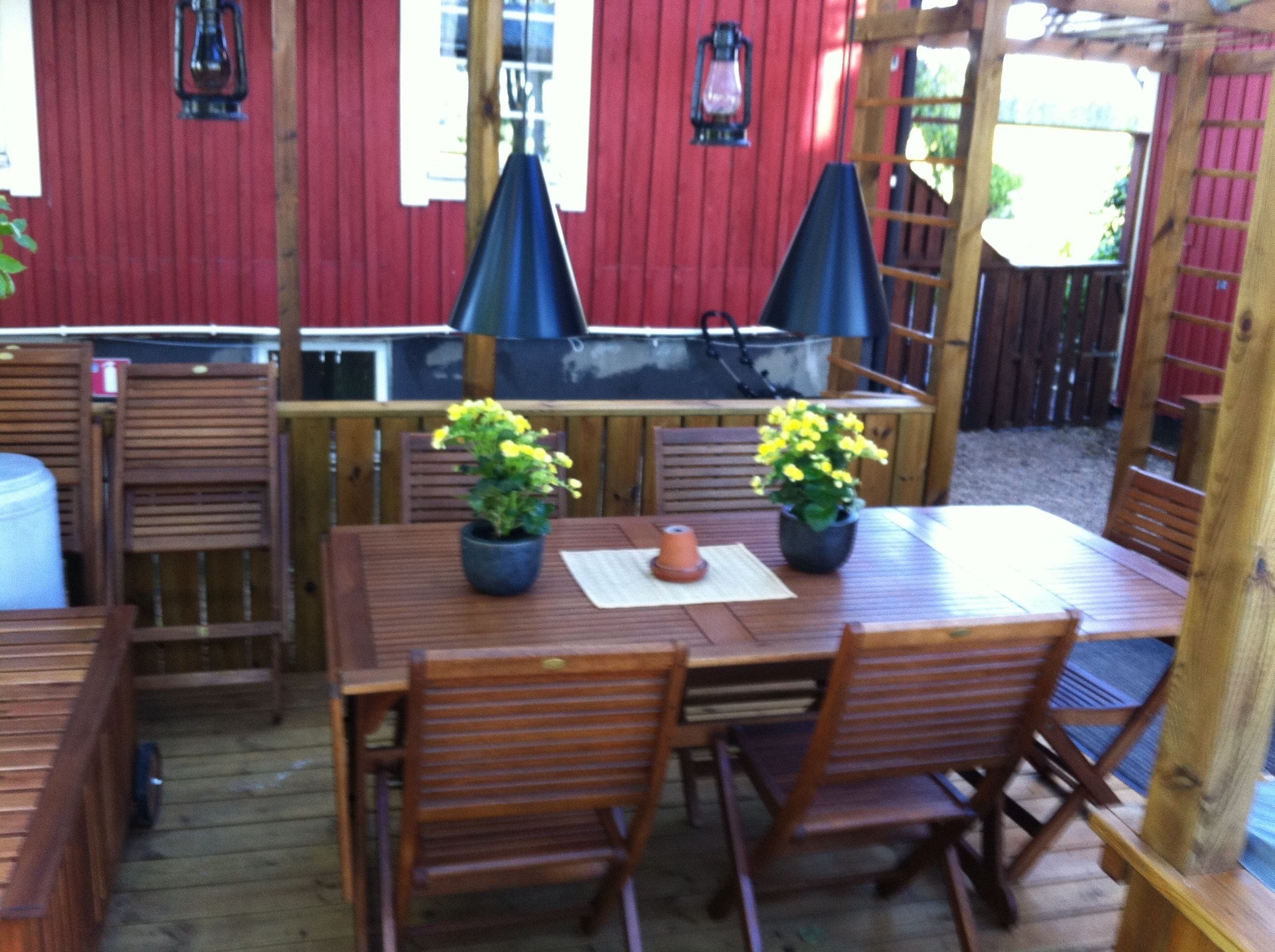 Eine Terrassengruppe im Freien mit Holztisch und Stühlen, zwei Blumentöpfen und einem Grill.