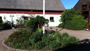 A building with a red and white facade, a gravel driveway, and a garden area with various plants and flowers. - Mattisgården Bed & Breakfast (Klippan)