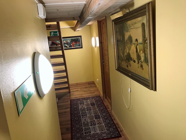 A hallway with a wooden staircase, a patterned rug, a framed painting, and a wall-mounted light fixture.