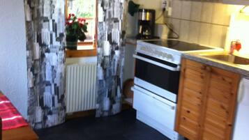 A compact kitchen with a stove, oven, and microwave. There is a window with patterned curtains and a radiator below it.