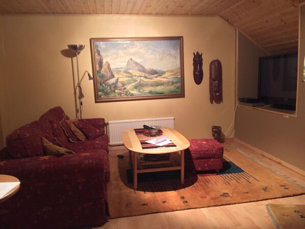 A living room with a red sofa, a wooden coffee table, a painting of a landscape, a floor lamp, and a television. - Mattisgården Bed & Breakfast (Klippan)