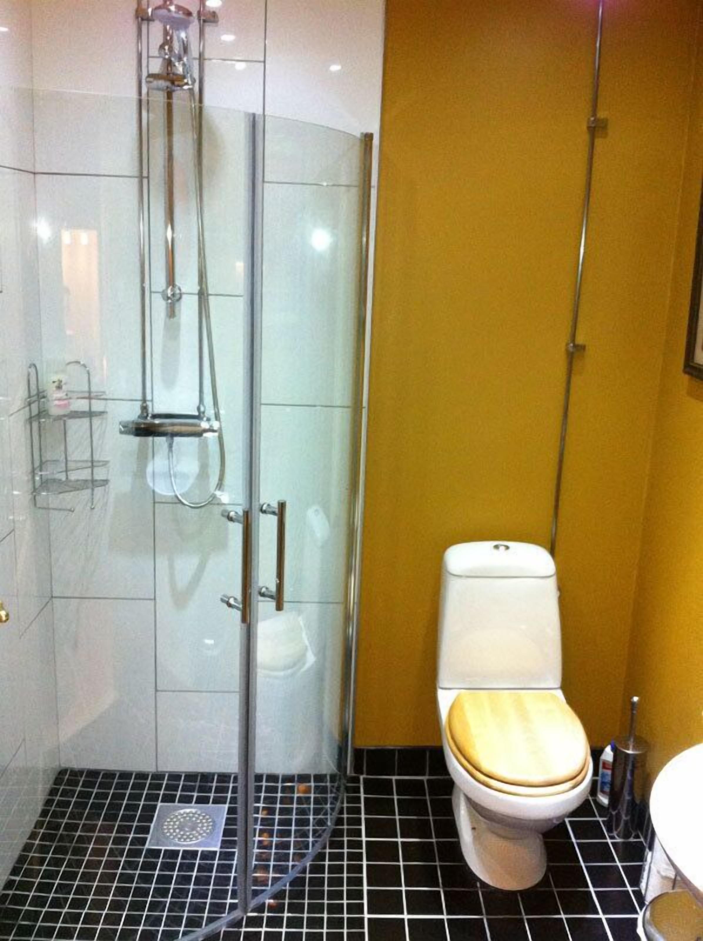 A bathroom with a glass-enclosed shower, a toilet with a wooden seat, and a tiled floor.