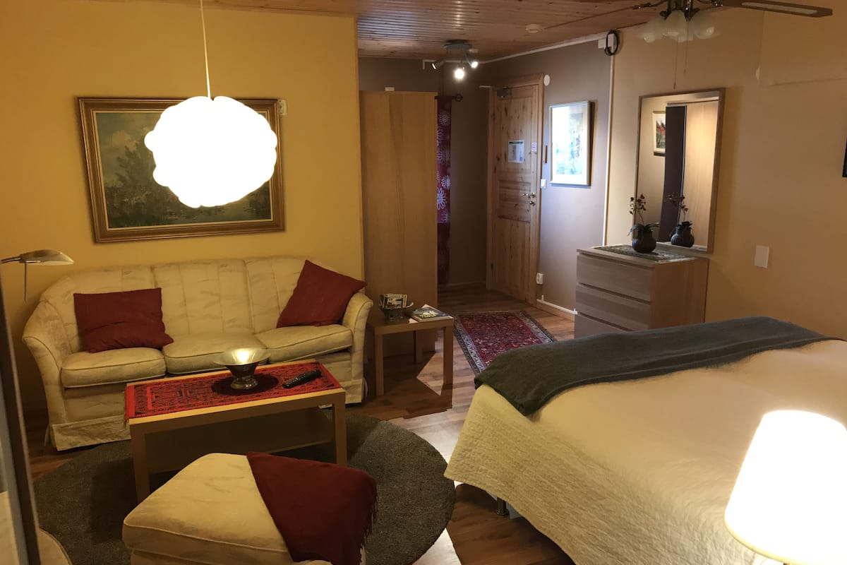 Ein gemütliches Zimmer mit einer Couch, einem kleinen Tisch mit einer Lampe, einem Bett und einer Holzbalkendecke.
