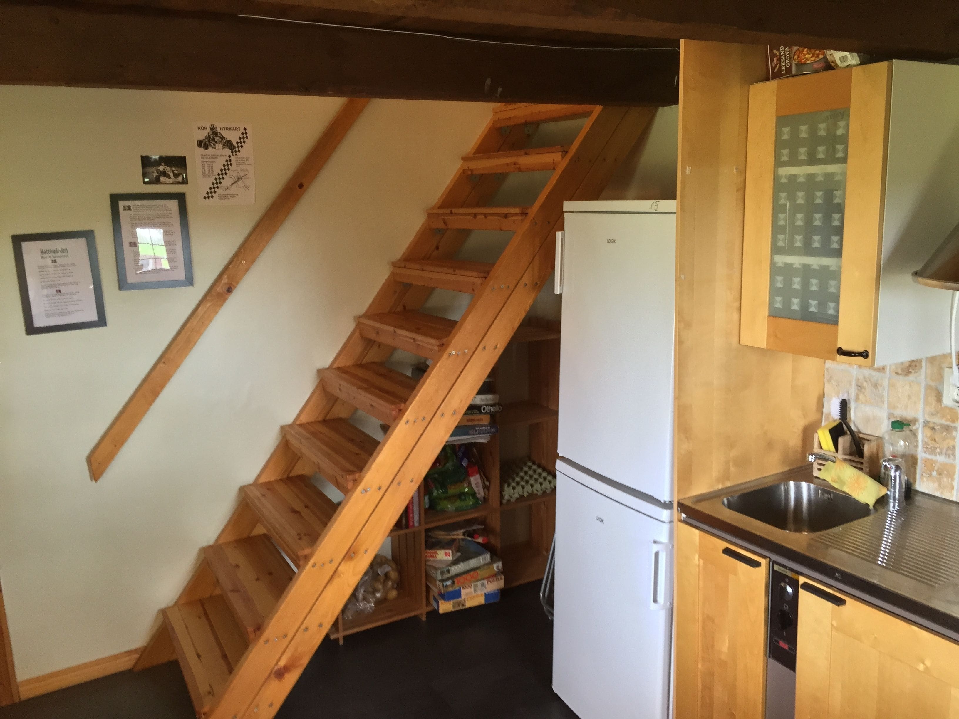 Una cocina con una escalera de madera, un refrigerador blanco y un lavamanos.