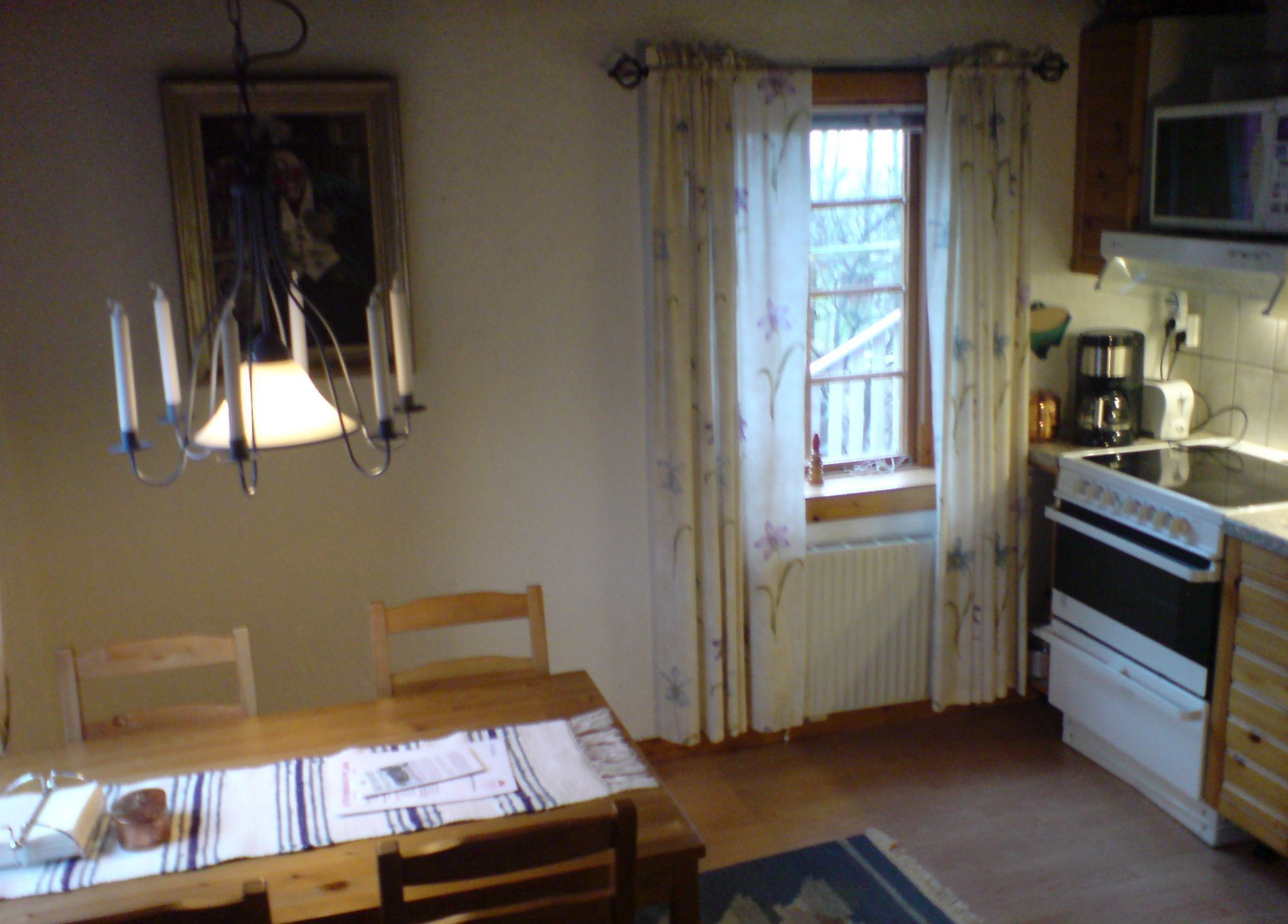 A small kitchen with a table, chairs, a window with curtains, a microwave, and a stove.