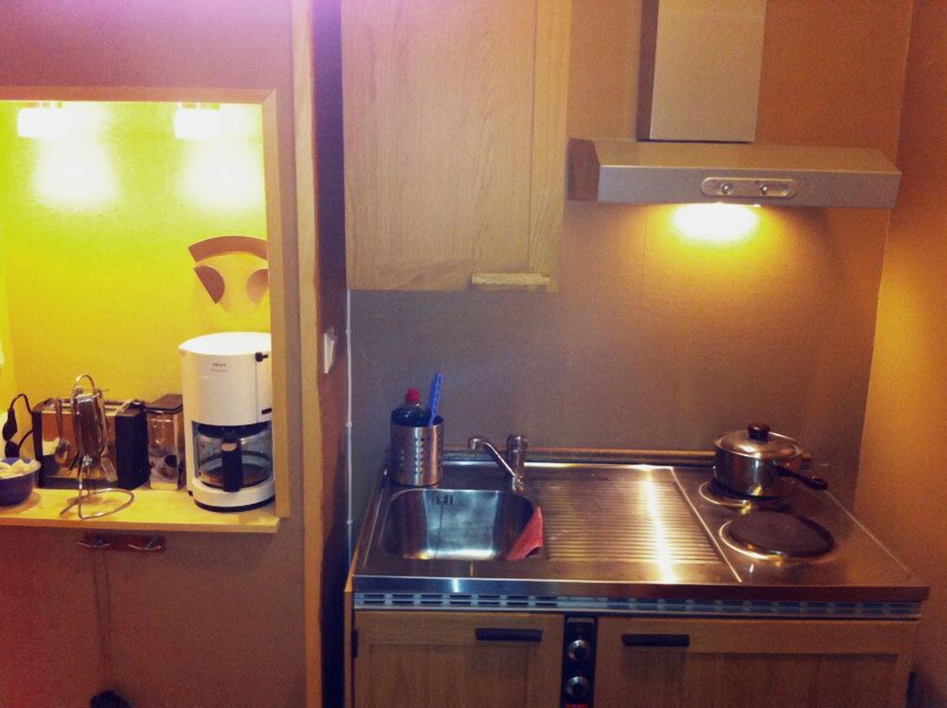 Una cocina compacta con cafetera, hervidor y estufa de acero inoxidable.
