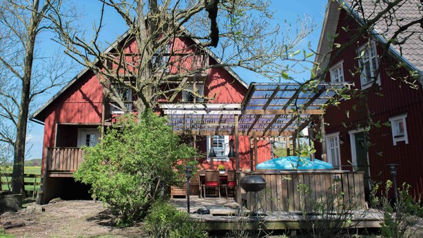 A red barn with a covered porch, a wooden deck, and a barbecue grill. - Mattisgården Bed & Breakfast (Klippan)
