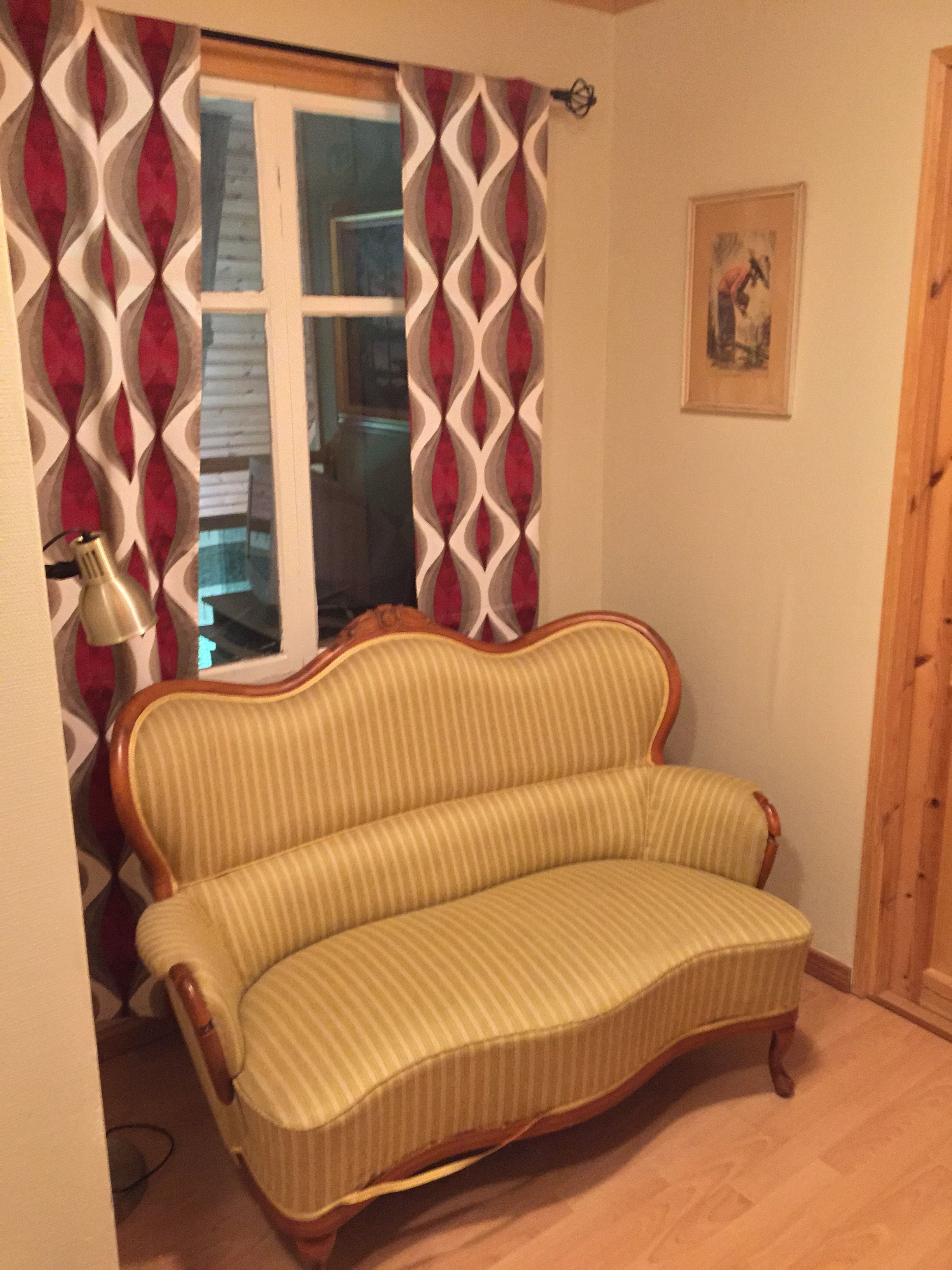 Una habitación con un sofá a rayas, una cortina estampada, una lámpara y un cuadro en la pared.