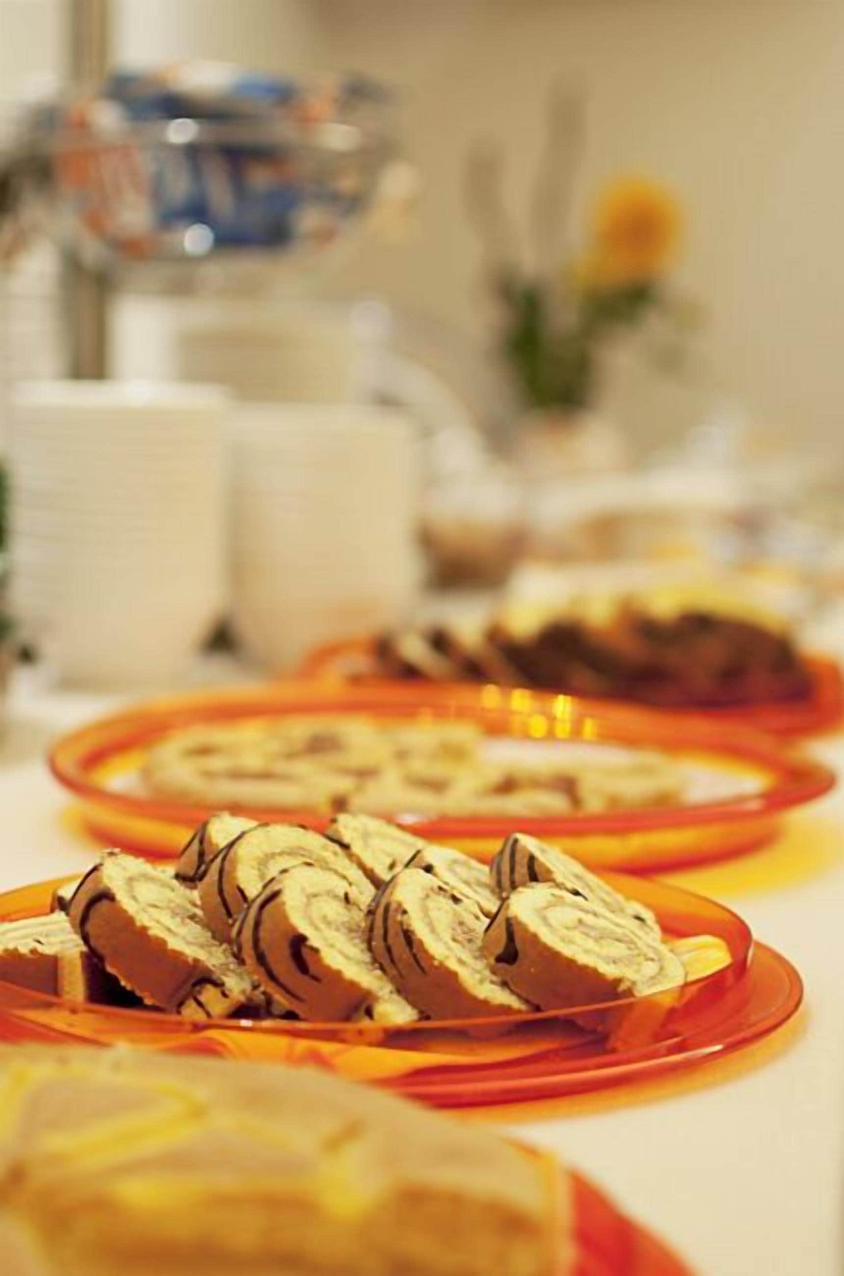 Ein Buffet mit verschiedenen Speisen, darunter Brötchen mit Schokoladenglasur, angeordnet auf orangefarbenen Tellern.